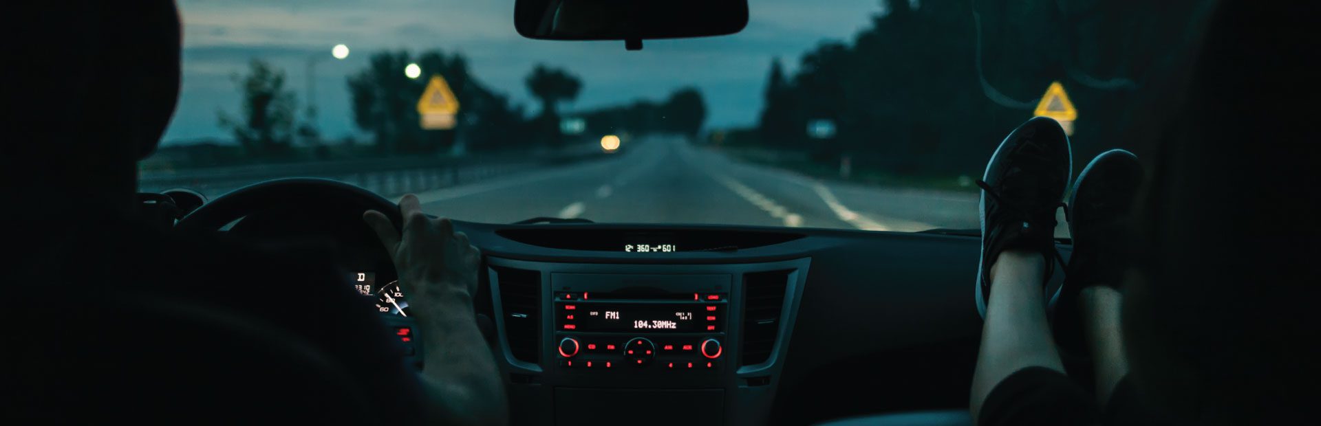 Two people traveling a night; the passenger puts her feet on the dash