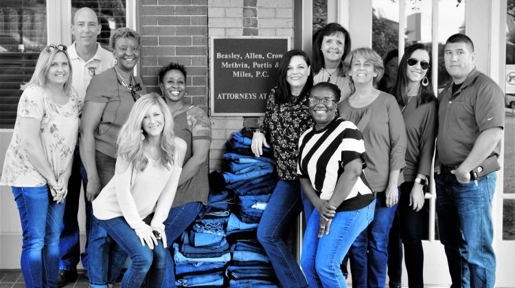 Beasley Allen employees wear blue jeans next to a stack of jeans to be donated to homeless shelter
