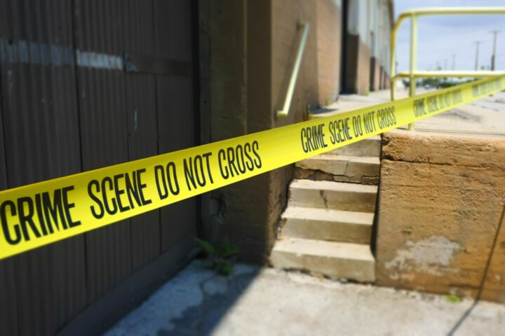Yellow tape stating "Crime Scene, DO Not Cross" on the outside of a building.