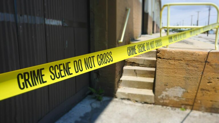 Yellow tape stating "Crime Scene, DO Not Cross" on the outside of a building.
