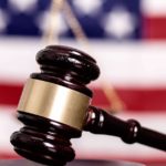 Gavel up close with scales of justice and American flag out of focus