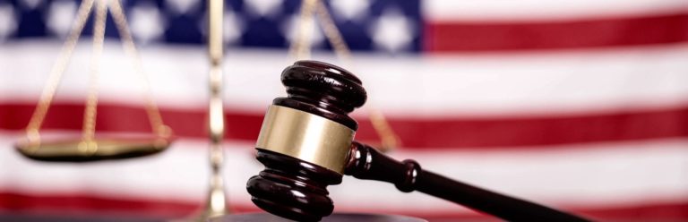 Gavel up close with scales of justice and American flag out of focus