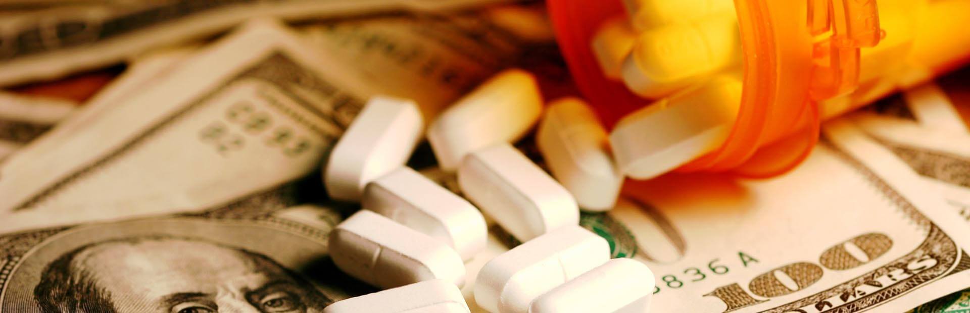White pills spilling out of a prescription bottle onto hundred dollar bills