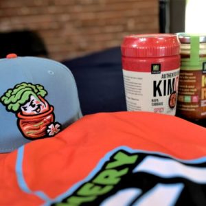 A close up of the uniforms worn by the Montgomery Kimchi among jars of Kimchi