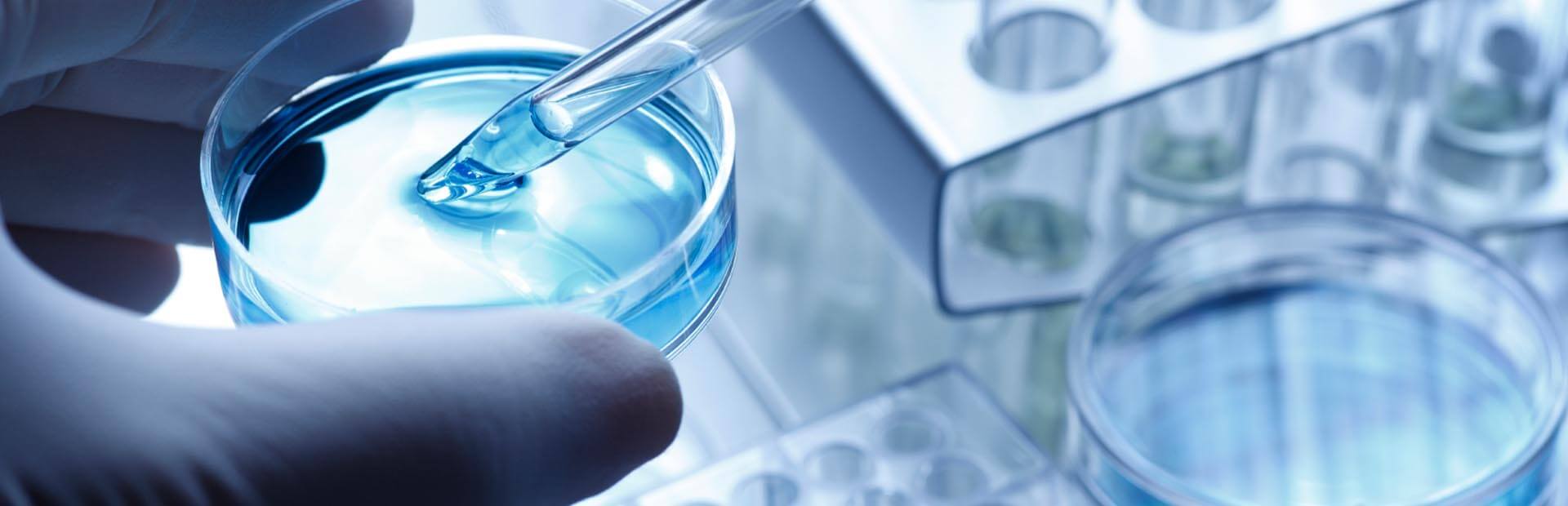 A lab tech testing a light-blue fluid in a petri dish