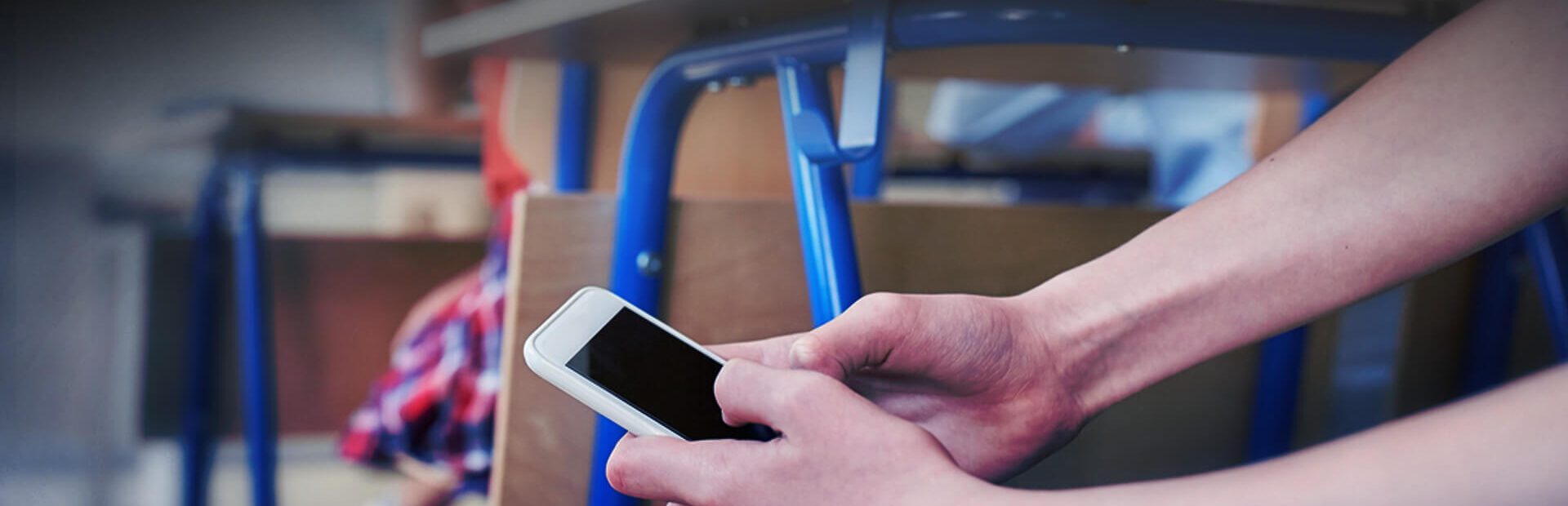 Student checks their phone secretly under a desk in a classroom