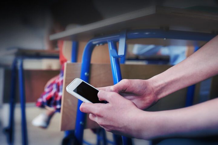 Student checks their phone secretly under a desk in a classroom