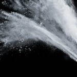Bottle of talcum powder shooting talc against a black backdrop