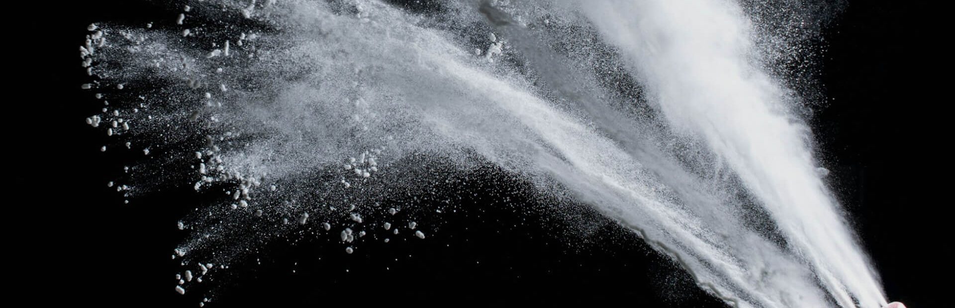 Bottle of talcum powder shooting talc against a black backdrop