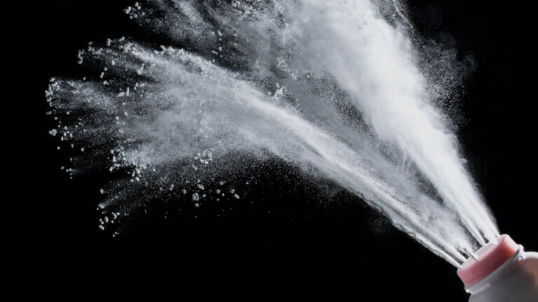Bottle of talcum powder shooting talc against a black backdrop