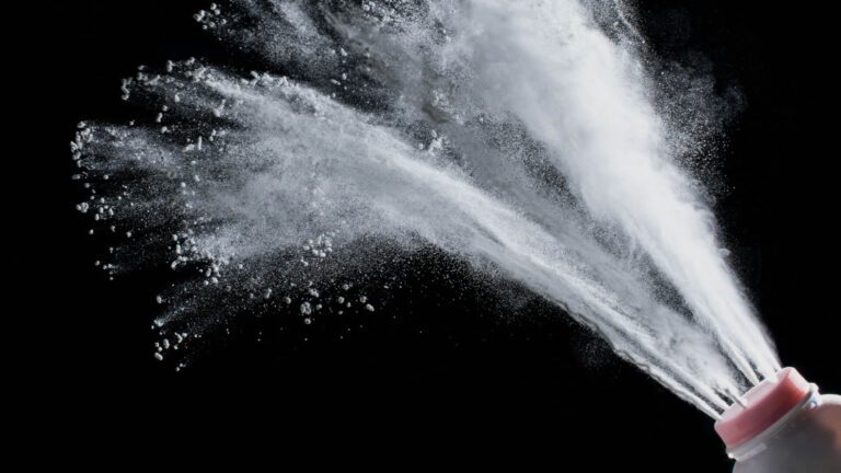 Bottle of talcum powder shooting talc against a black backdrop